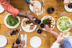 A top down view of people clinking glasses above a table of food.