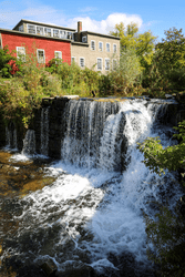 Water cascades down a waterfall, surrounded by green vegetation on a warm sunny day.