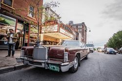 A vintage car parked in front of a historic theatre with a marquee that reads Flynn.