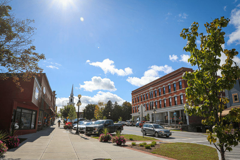 A street is lined by old brick buildings on both sides on a warm sunny day.