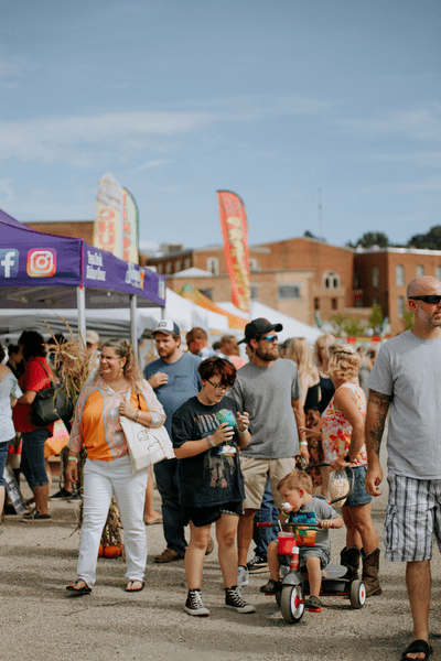 Group of people walk around an outdoor festival on a sunny day.