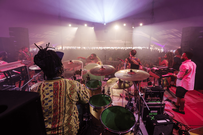 As seen from behind, a musical group plays a concert from a lit performing stage.