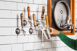 A beer tap pours beer into a metal cup in a person's hand.