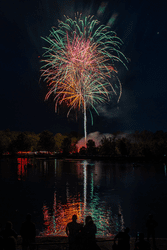 Fireworks shoot into the sky at night sky with a reflection in water below.