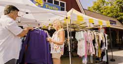 People shop racks of clothes under tents outdoors.