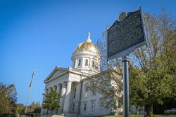 A historic roadside marker sign commemorating marriage equality for same-sex couples in front of the golden dome of the Vermont Statehouse.