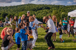 A person plays a guitar for dancing spectators outside on a warm day.