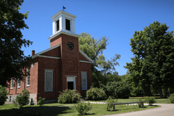 A brick building with a clock on a sunny day at an outdoor museum.