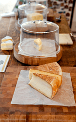 Two wedges of cheese on a wooden plank inside a store.