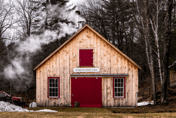 A wooden building with red doors has steam and smoke emitting from a chimney.