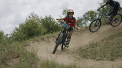 An adult and a child mountain biking outside in the summer.