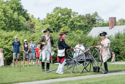 People dressed as Revolutionary War soldiers outside reenact history for a crowd.