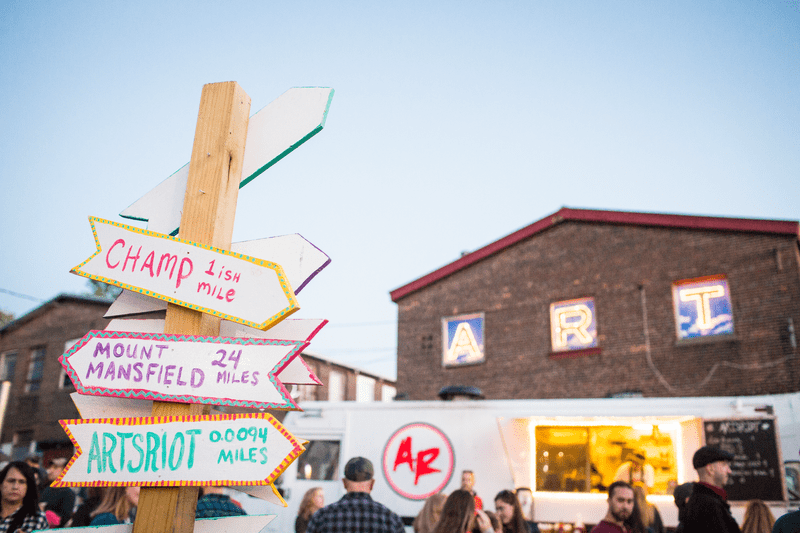 A wayfinding sign sits in front of a food truck at an outdoor event.