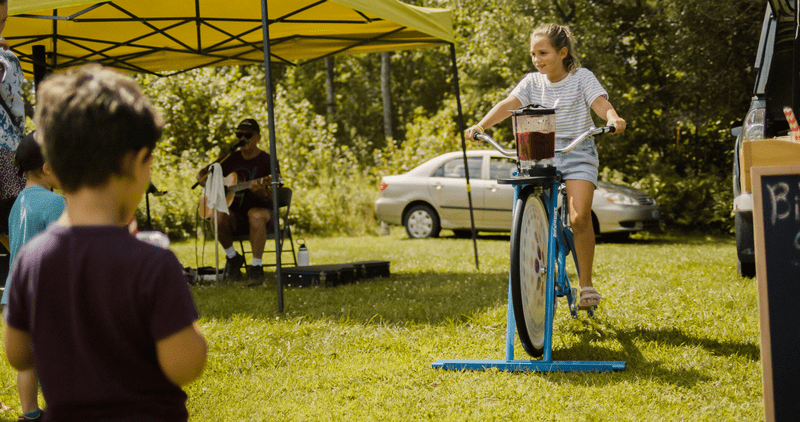 A child pedals a stationary bike that is connected to a blender