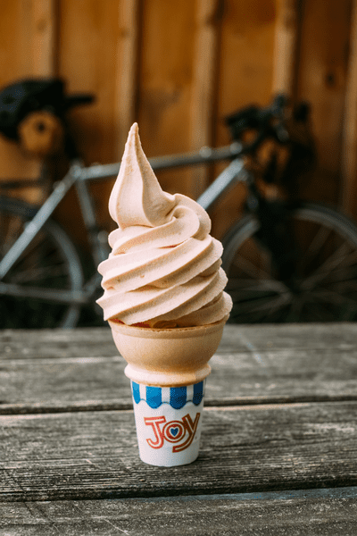 A cone with pink soft ice cream sits on a wood picnic table.