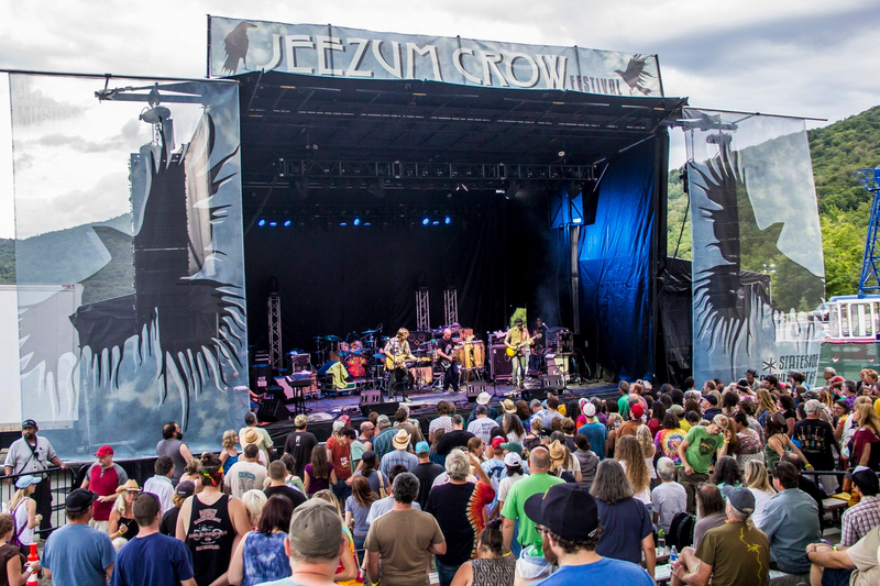 A crowd gathers around an outdoor stage to watch a band during late afternoon.