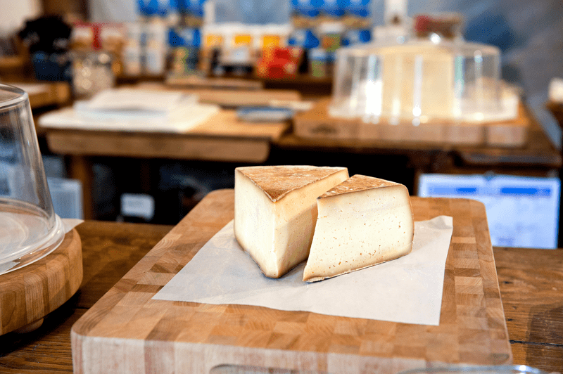 Two wedges of cheese on a wooden plank inside a store.