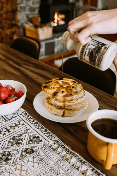 A hand pours maple syrup on pancakes.