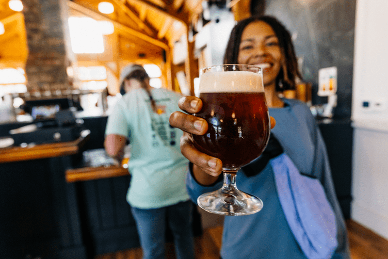 A person holds a pint of beer towards the camera.