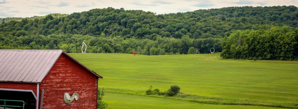 A red building next to a wide field of green grass. Sculptures sit in the distance.