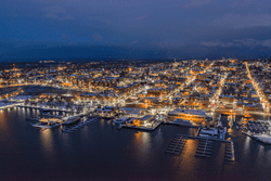 Seen from above, a lit-up city at night next to a lake.