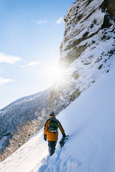 A person walks through deep snow on the side of a mountain.