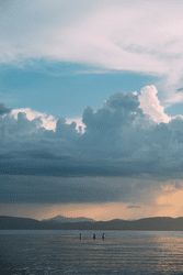 In the distance, three people are in a lake with mountains in the back.