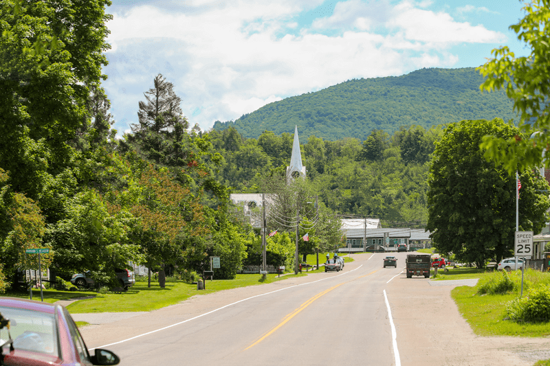 A road leads through a historic downtown with a white church and cars on the road.