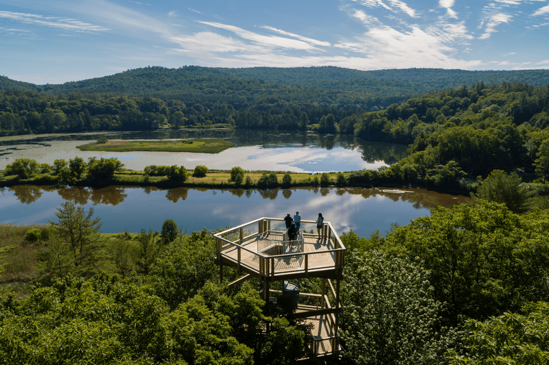 Four people stand on a platform overlooking a scenic view of a river and mountains.