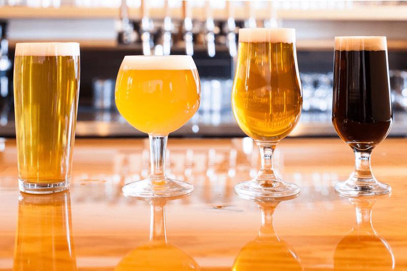 Four beers are poured in glasses on a bar.