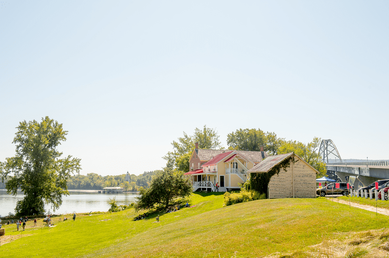 A historic site on a field with a lake and a bridge behind.