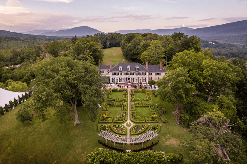 A historic mansion seen from above in the summer, nestled between mountains.