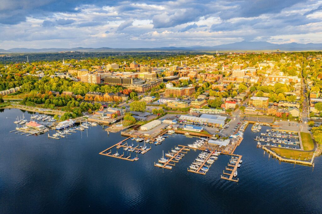 Seen from above, a sprawling rural city lines a large body of water in the setting sun.