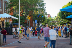 Groups of people shop an outdoor marketplace in warm weather.