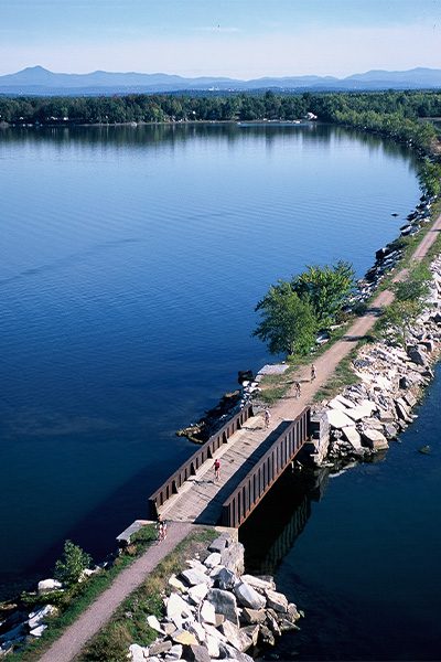 Ariel view of a causeway topped with a gravel path and a bridge over a channel of water.