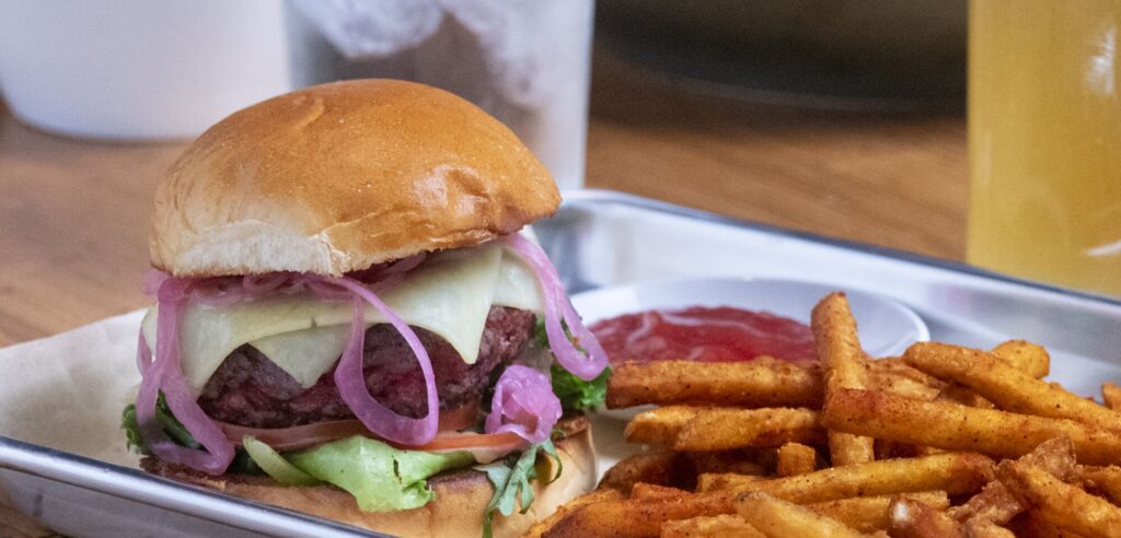 Table with a hamburger, fries, pickles, and ketchup on a steel plate.