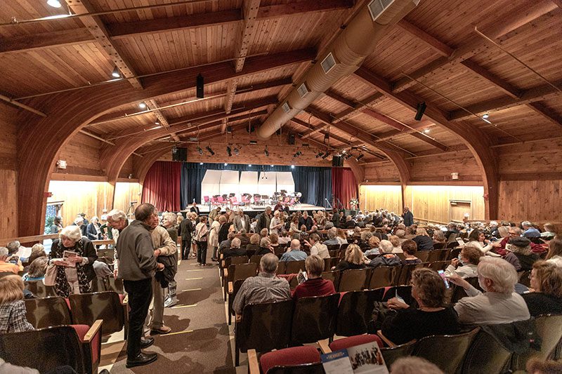 Indoor view of a music venue with wooden walls and ceiling, and stage for performers in the background.