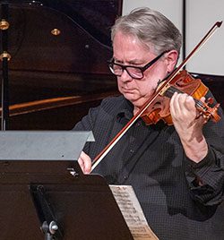 A man plays a violin with sheet music on a stand in front of him.