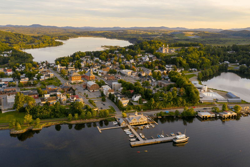 A large lake surrounded by mountains with a downtown on the shore, as well as docks and boats.