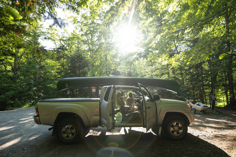 A truck with a canoe on top and a person loading gear.