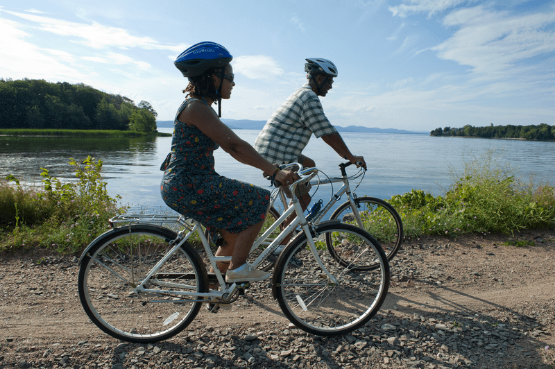 Two people ride pikes on a gravel path next to a lake.