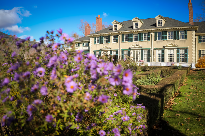 A historic mansion seen from its garden under a bright blue sky.