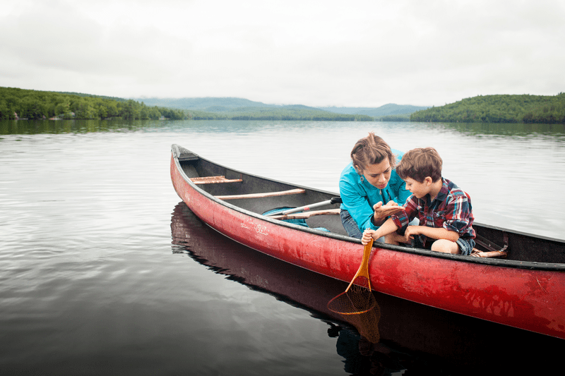 An adult and a child fish from a canoe.