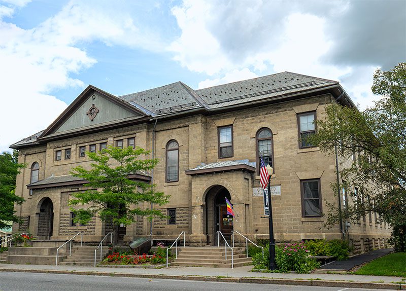 A brick building with a rainbow flag and an American flag seen from outside in the summer.