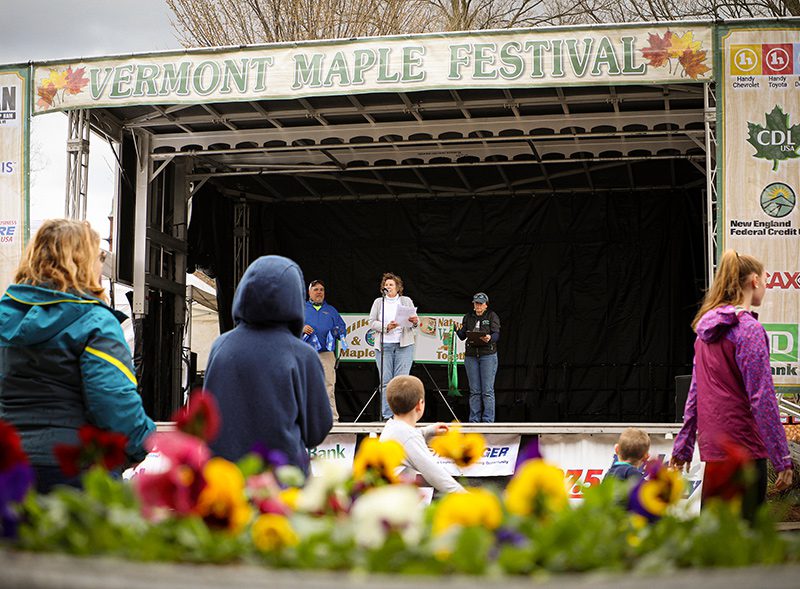 Yellow flowers bloom under a stage where live music is being performed for a small crowd.