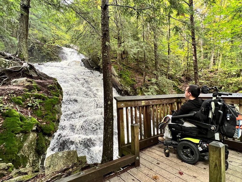 A person in a wheelchair seen from behind as they look at a waterfall view.