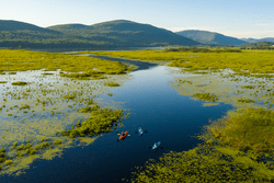 Ariel view of three kayakers paddling down a meandering river, surrounded by mountains.