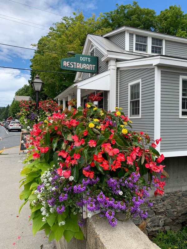 Red, purple, and yellow flowers sit on a bridge railing with a building behind.