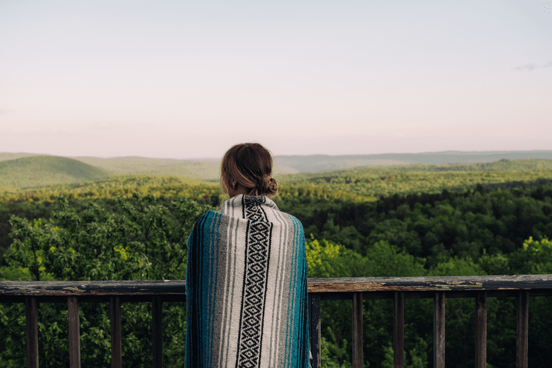 A person looks out over a mountain view with green trees visible on hillsides.