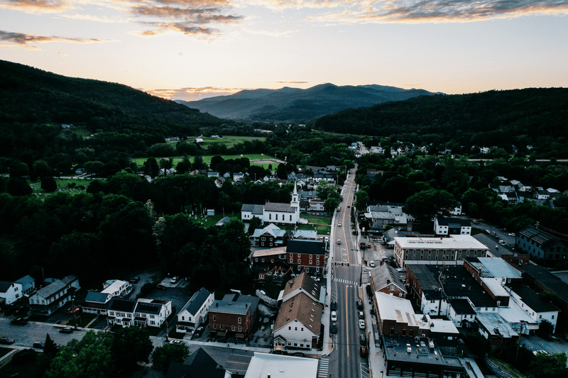 Seen from high above, a downtown in a valley between mountains. The sun is setting between mountains in the background.